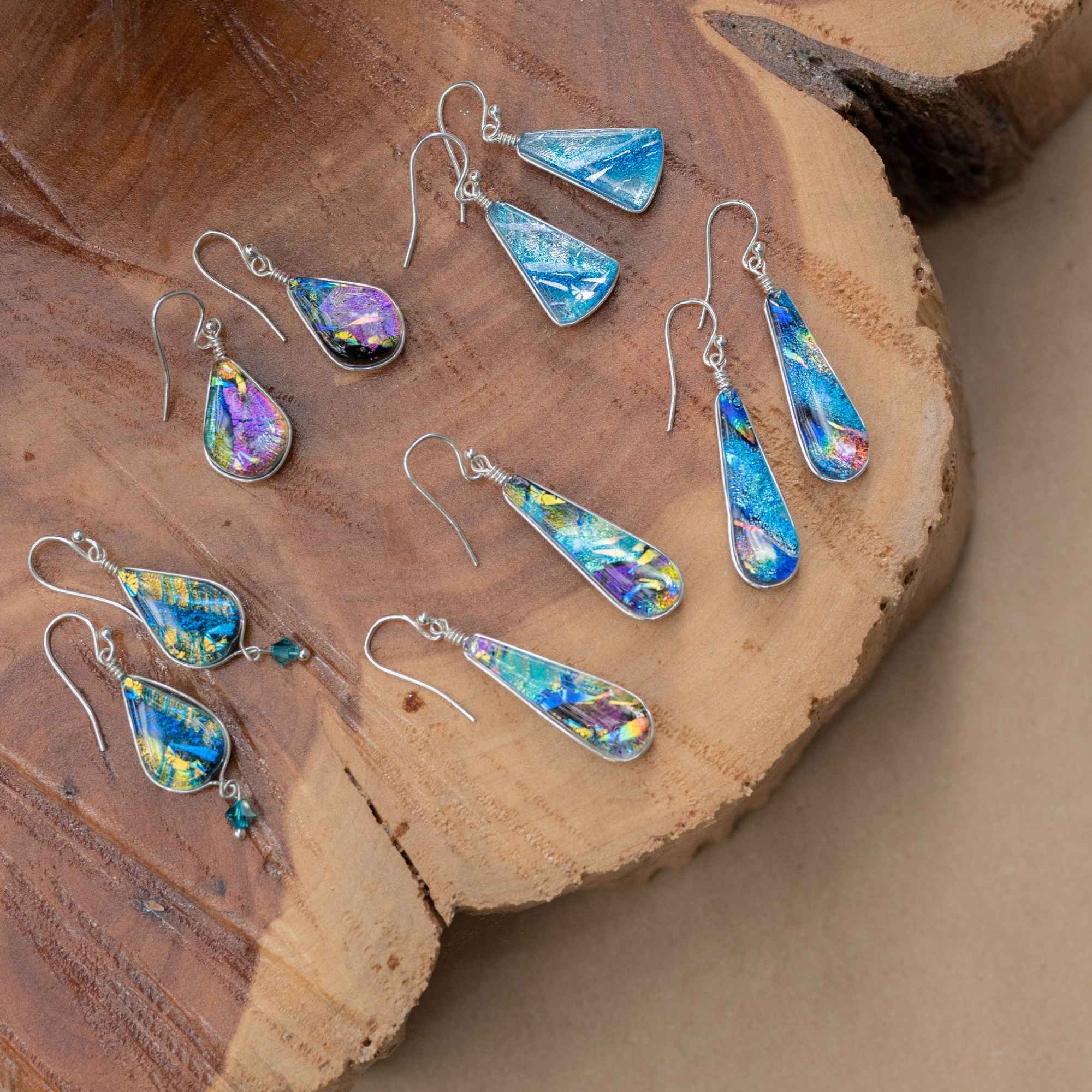 Five pairs of colorful dichroic glass earrings, featuring the Rainbow Falls, on a wooden platter.