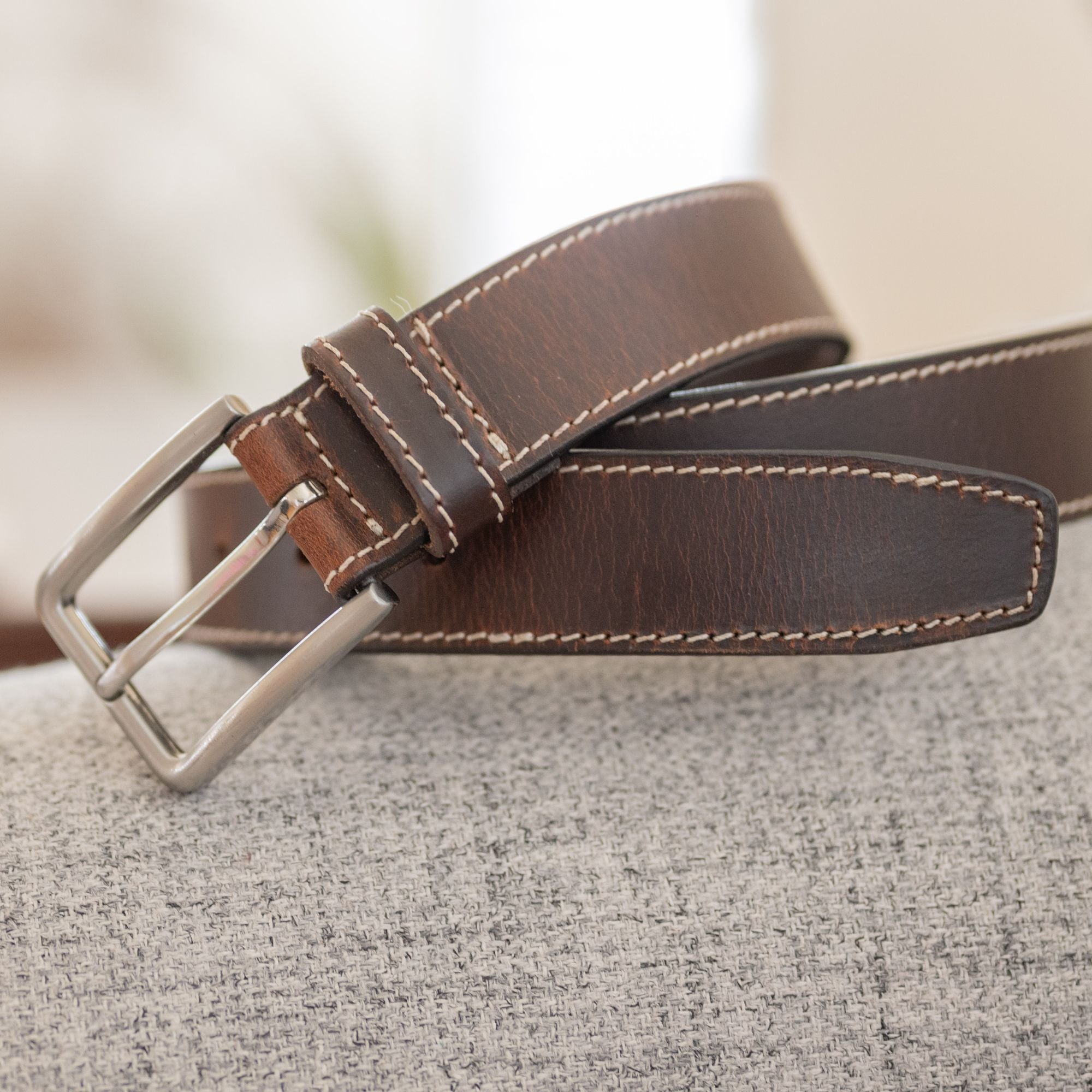 Slick City Brown Belt on a couch. Cream stitch, tapered end. Silver buckle.