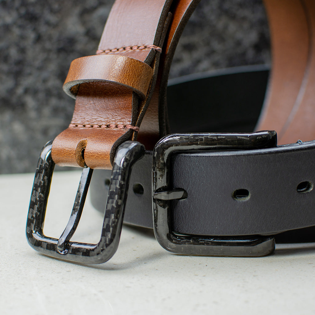 Image of 2 belts. One black leather and one brown leather. Both have black carbon fiber buckles and are TSA Friendly