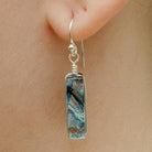 Multicolored silver earring in a rectangular shapee worn on an ear.