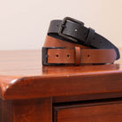 Two leather belts, one brown and one black, on a wooden surface.