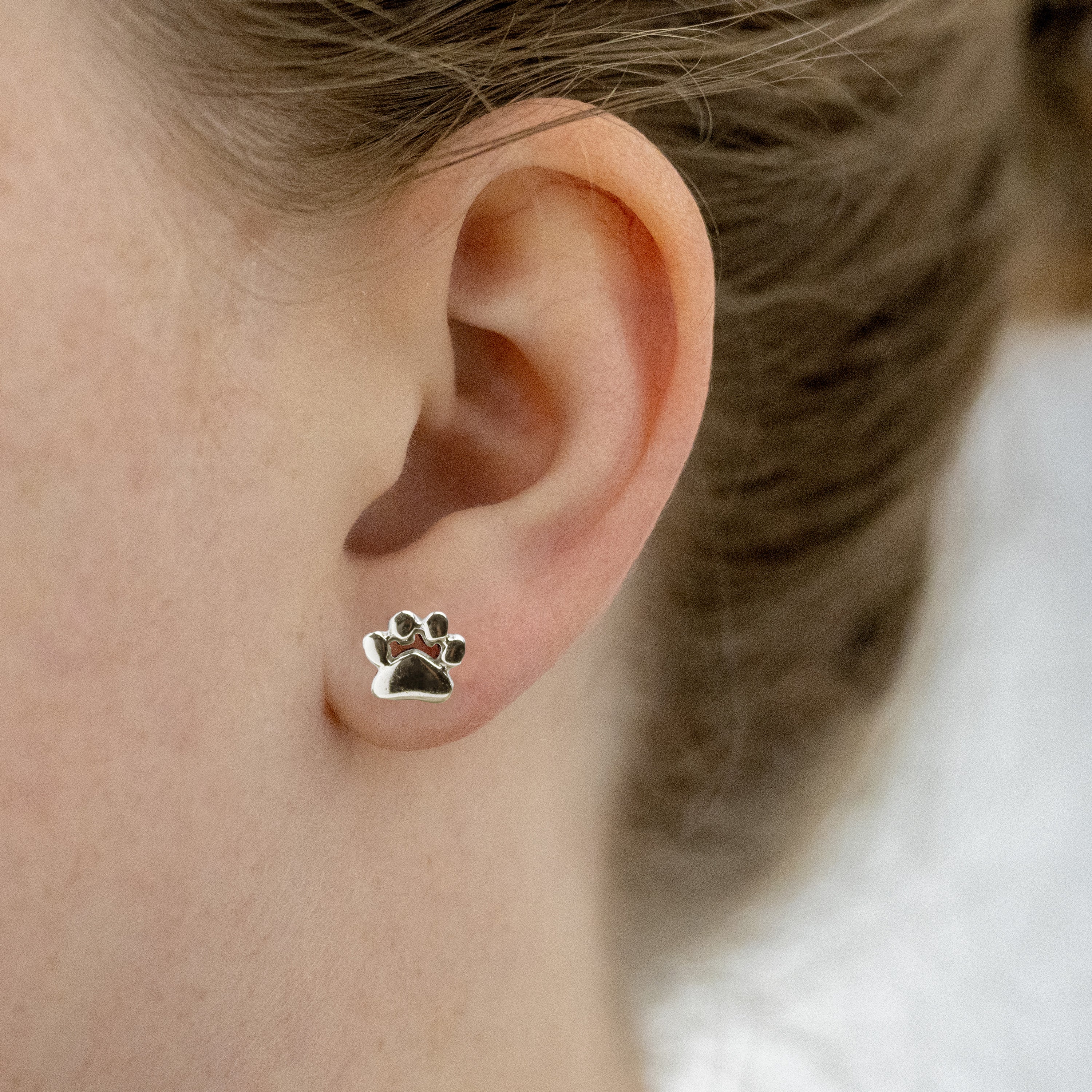 Bright shiny paw print earring on a model.